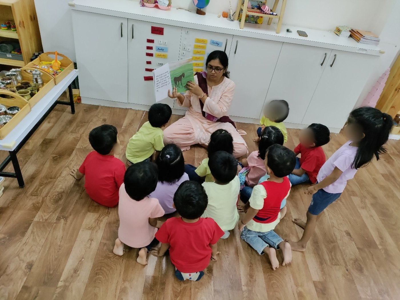 An educator holds up a book while young children sit around her