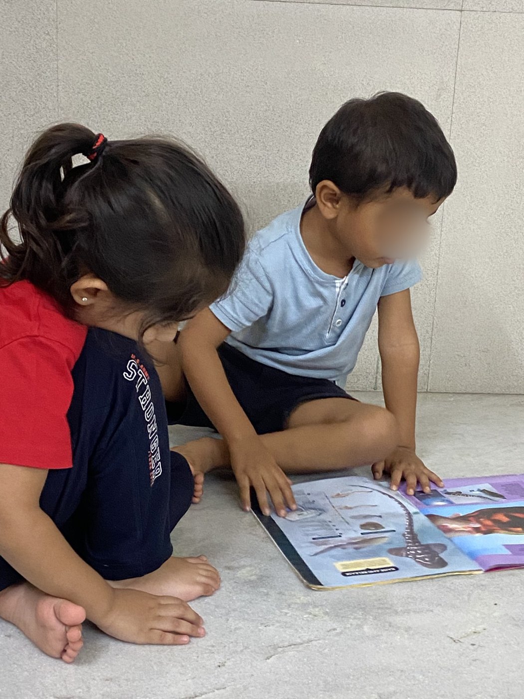 Two children look at a picture book together on the floor