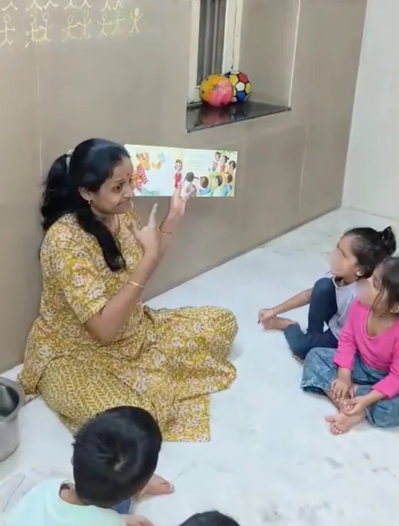 An educator shows a picture book to young children and acts out the story with her hands